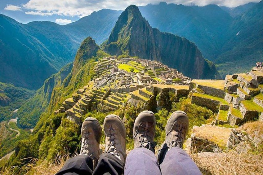 En person sidder med krydsede ben og ser ud over ruinerne af Machu Picchu. 1
