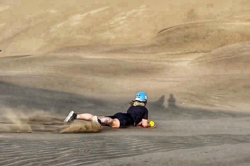 A person lying on the ground in a sandy area, wearing a helmet and holding a yellow object. 5