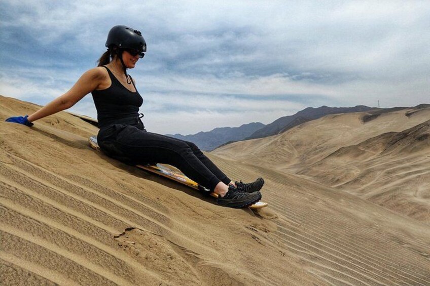 A person sliding down a sandy slope with a helmet and goggles, surrounded by a vast desert landscape. 2