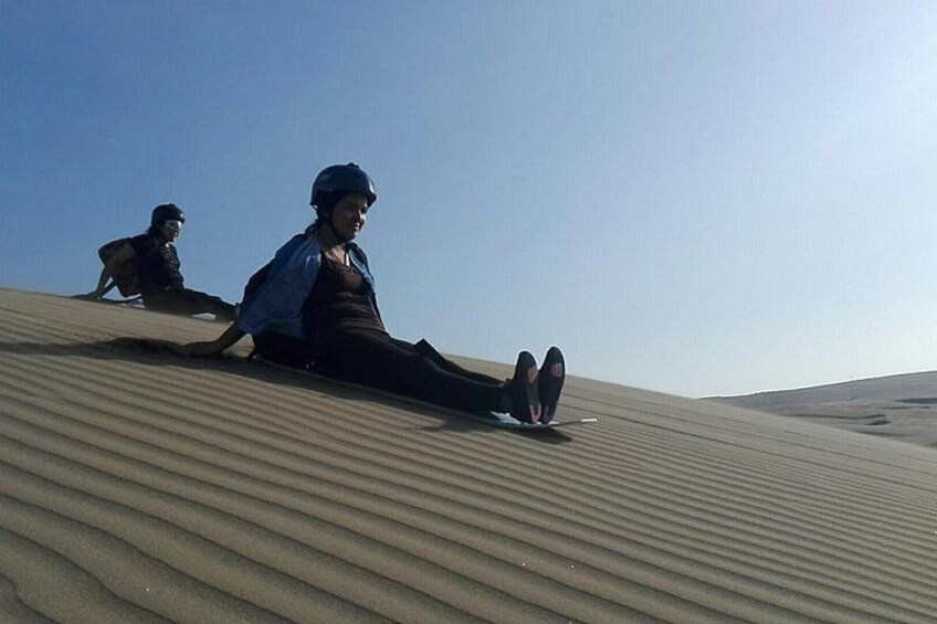 Two people sitting on a sand dune with a clear sky. 1