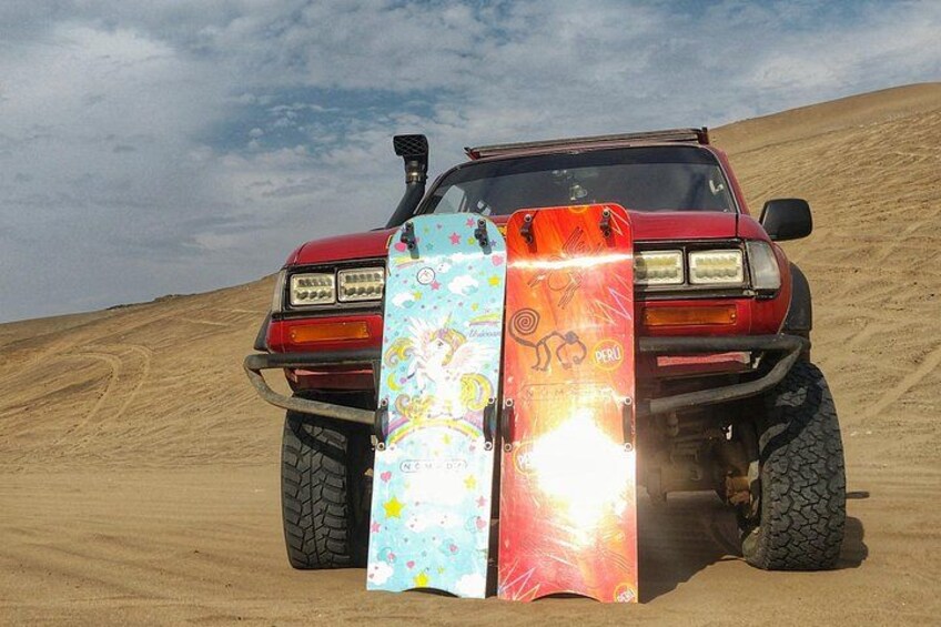 A red off-road vehicle with two surfboards on its front bumper, parked on a sandy dune. 3
