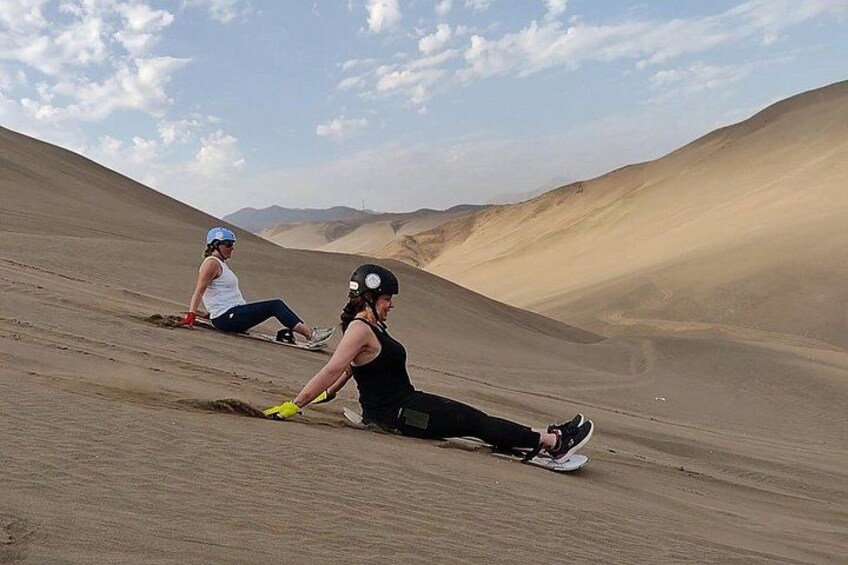 Two people sledding down a sand dune in a desert landscape. 4