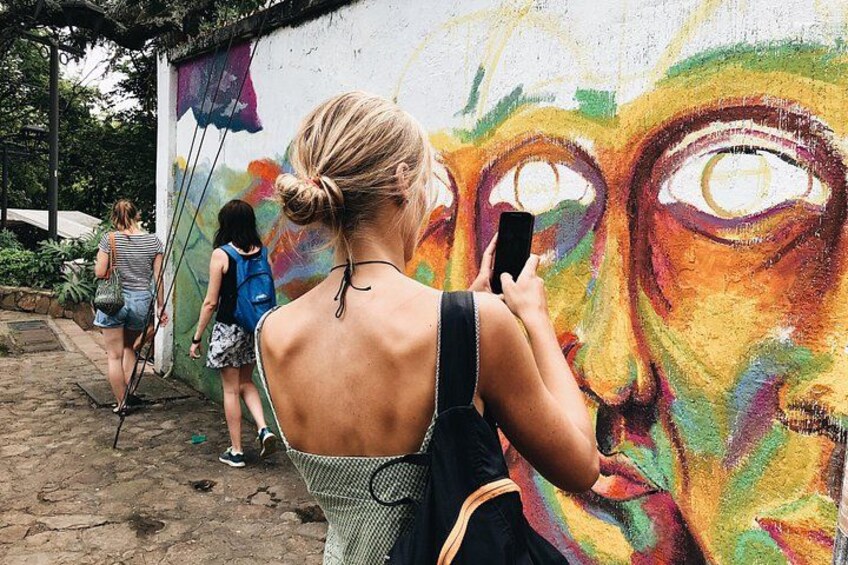 Un mural en una pared, una persona fotografiando y otra caminando. 2