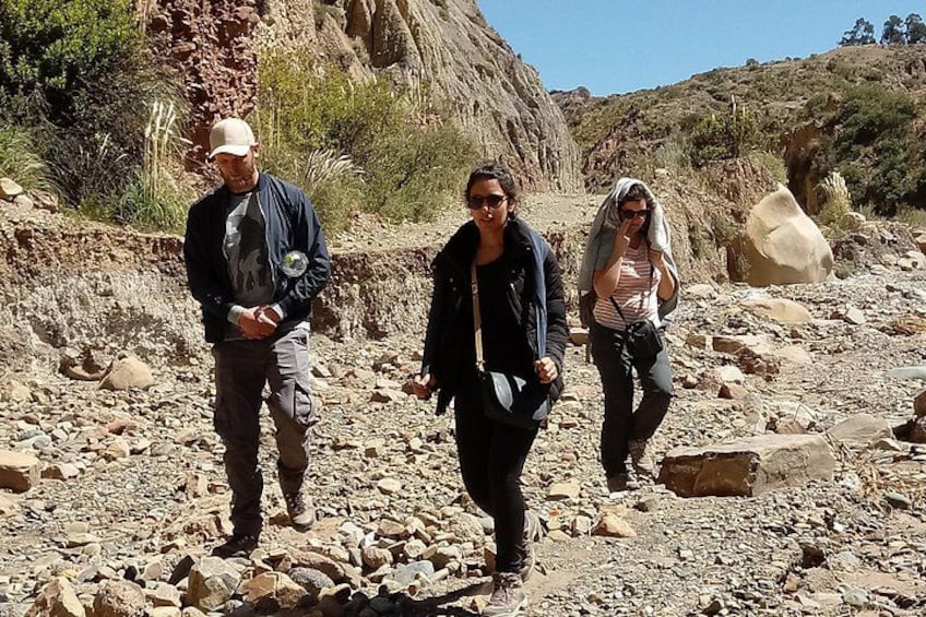 Tres personas caminando por un sendero pedregoso en un paisaje desértico con poca vegetación y terreno rocoso. 5
