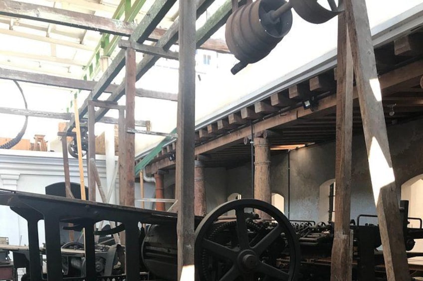 Ein historischer Industrieort mit freiliegenden Maschinen, Holzbalken und einem großen Rad. 3