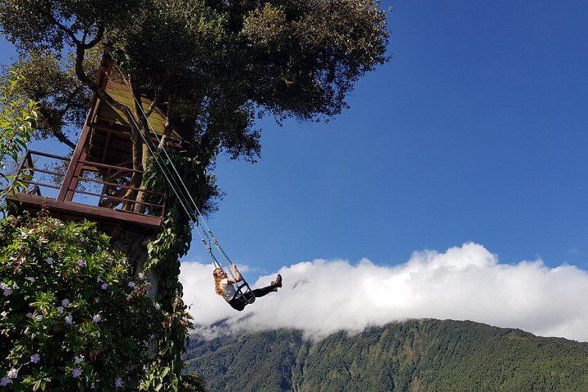 Une personne se balance à l’aide d’une corde, suspendue à une plateforme en bois, et surplombe un paysage montagneux où les nuages flottent en contrebas. 4