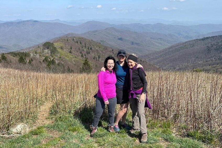 Cuatro personas de pie en una colina cubierta de hierba, con un paisaje montañoso al fondo. 2