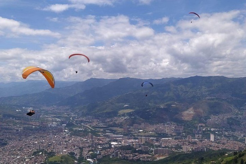 Paesaggio urbano con montagne sullo sfondo e diversi parapendisti in volo. 2