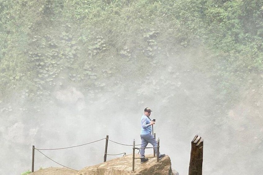 Una persona de pie sobre una roca con una barrera de cuerda, rodeada de un área boscosa. 4