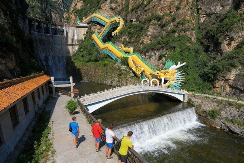 Eine Drachenstatue auf einer Brücke über einem Wasserfall, in der Nähe gehen Menschen vorbei. 2