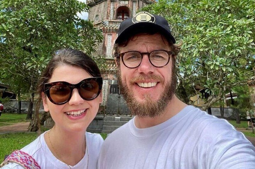 A man and a woman taking a selfie in front of a historical building with steps and greenery. 3