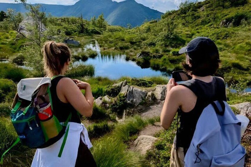 Dos personas caminando por la montaña cerca de un lago rodeado de vegetación. 1