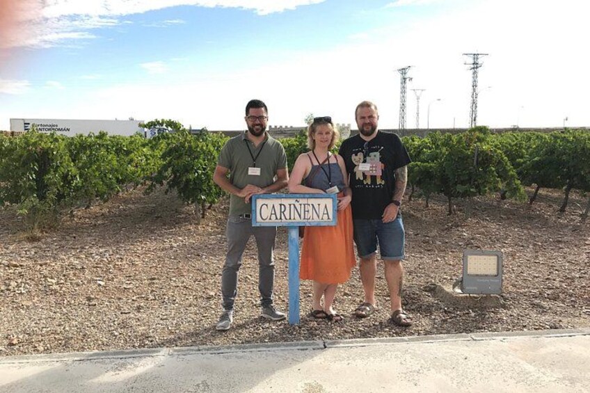 Tres personas de pie frente a un cartel que dice 'CARINENA' en un viñedo. 2