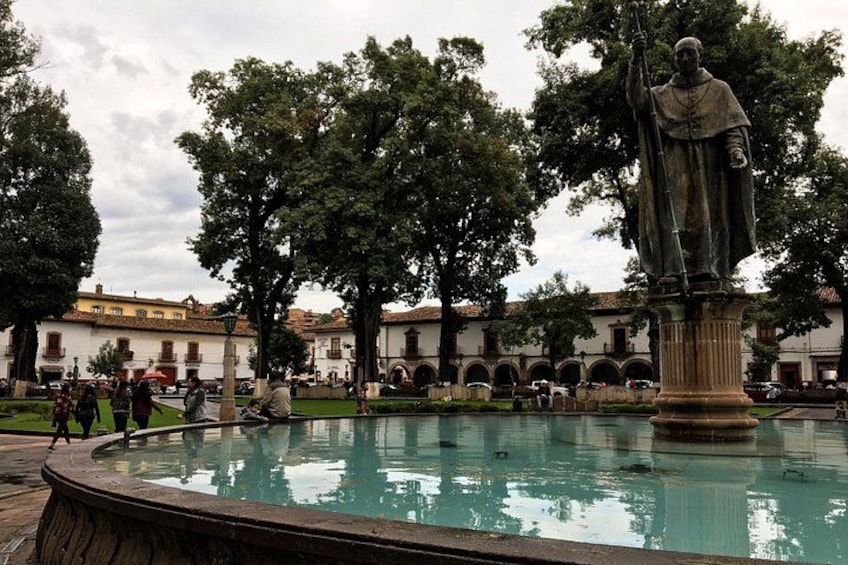 Une statue se dresse sur une place, près d’une fontaine, et est entourée d’arbres et d’immeubles. 4
