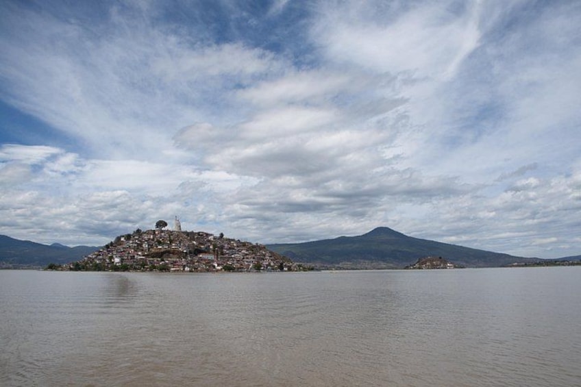 Un lac paisible avec une petite île sur laquelle se trouve un bâtiment imposant, et une montagne en arrière-plan. 1
