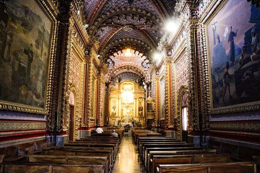 An ornate church interior with rows of pews, a central altar, and detailed wall paintings. 1