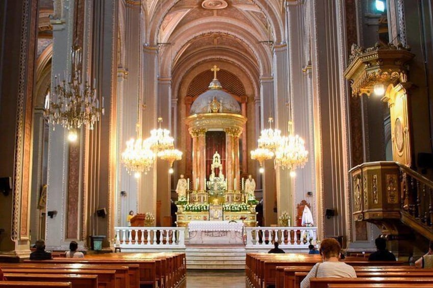 An ornate church interior with a central altar, pews, and chandeliers. 2