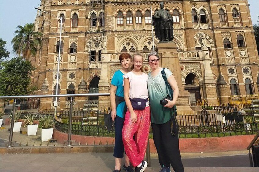 A group of people standing in front of a large, ornate building with intricate architectural details and a statue on top. 2