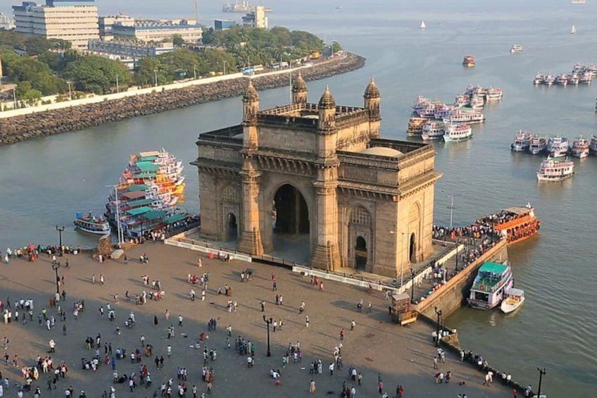 The Gateway of India, a historic monument, with a busy promenade and boats in the background. 1