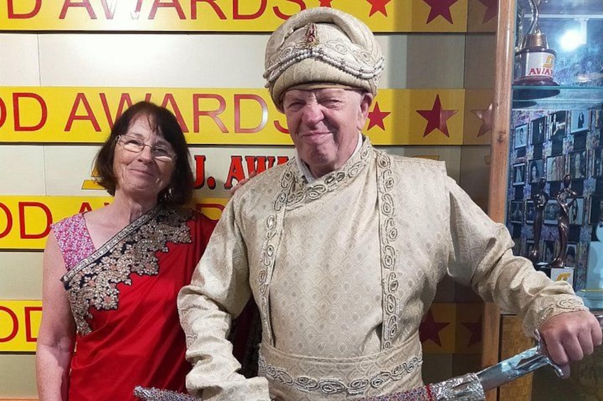 Una persona vestida con traje tradicional sostiene una espada, de pie frente a un fondo con texto y estrellas. 2