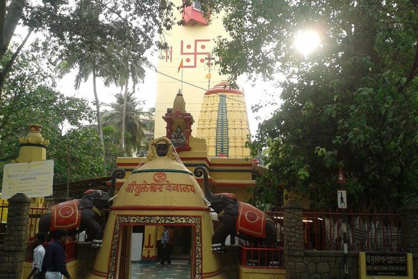 A temple with a large statue, a red and yellow entrance, and a signboard. 4