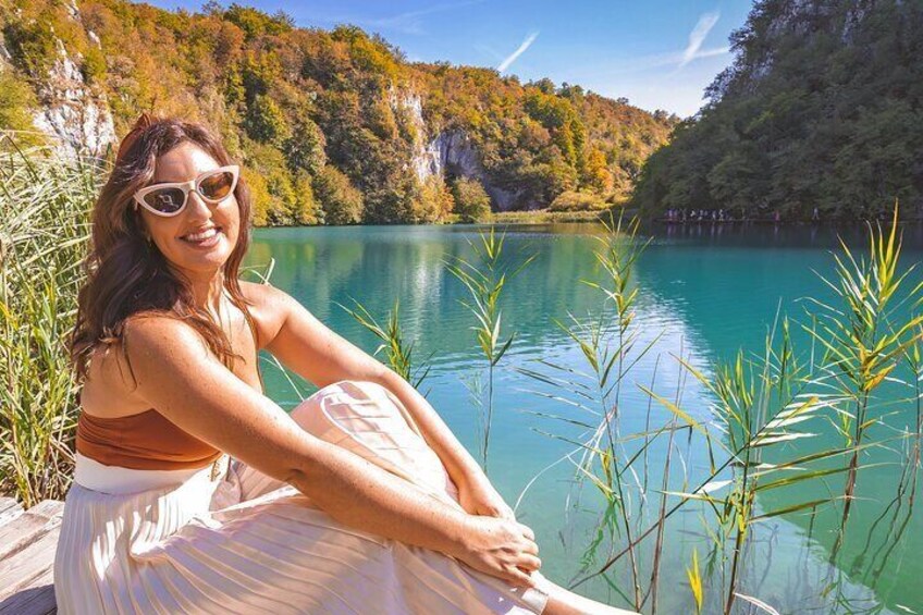 A person sitting by a lake with clear water, surrounded by greenery and hills. 5