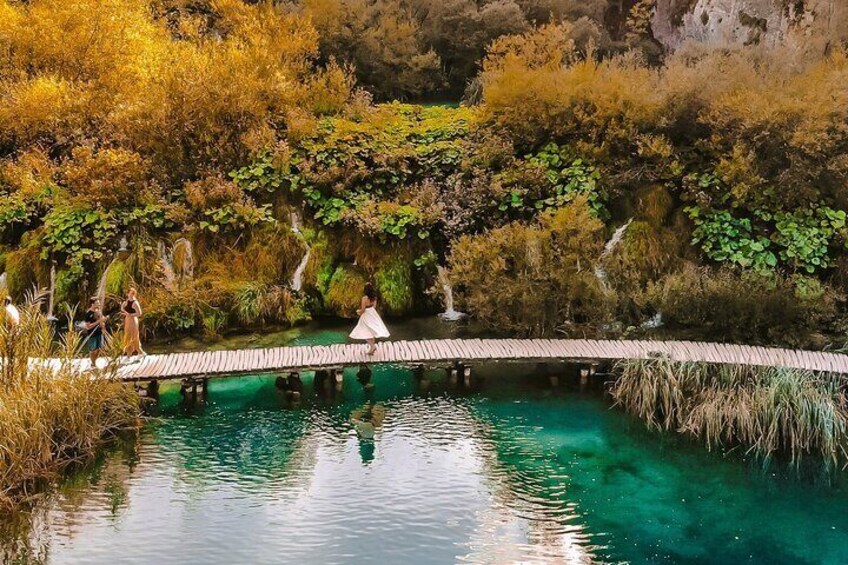 A wooden bridge over a clear blue pond surrounded by autumn foliage. 1