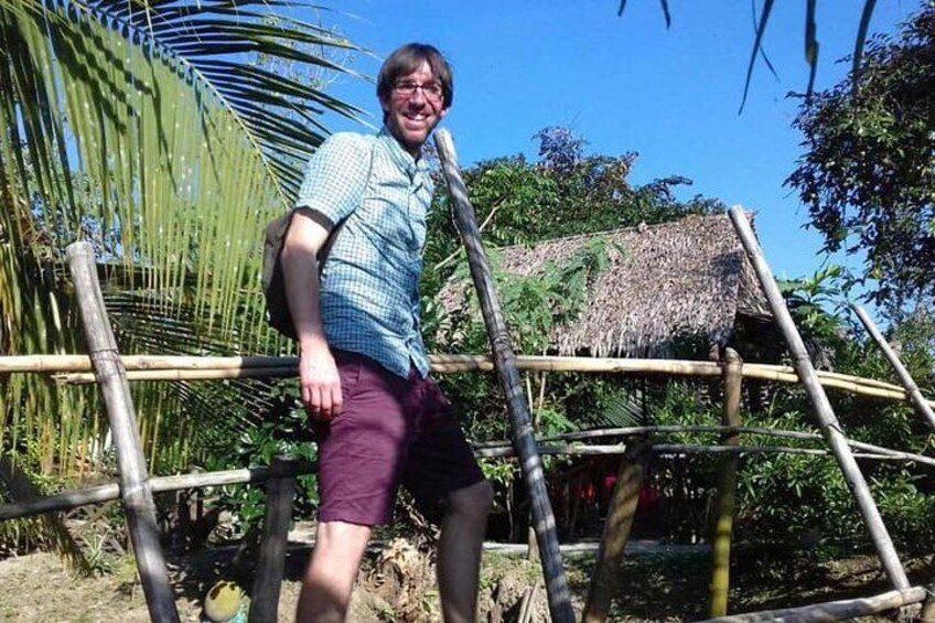 Una persona de pie junto a una estructura de bambú con techo de paja, rodeada de follaje tropical. 2