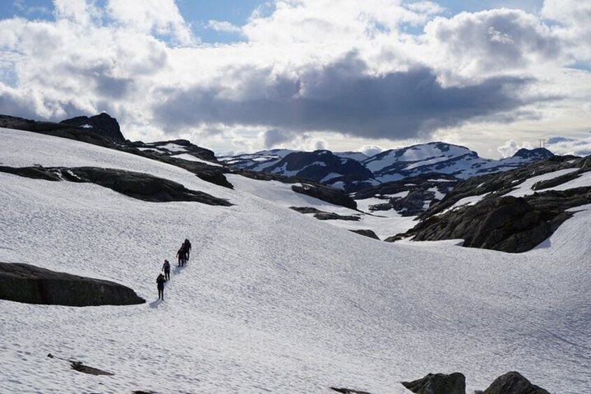 Un groupe de randonneurs sur un sentier de montagne enneigé, avec un terrain rocheux et des sommets enneigés au loin, sous un ciel partiellement nuageux. 5