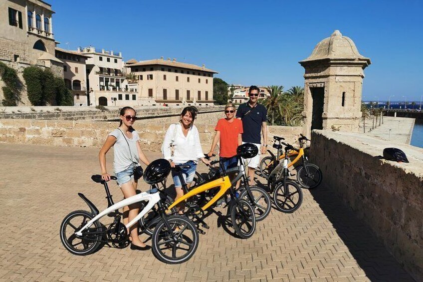 A group of people posing with bicycles in front of historical buildings and a port. 1