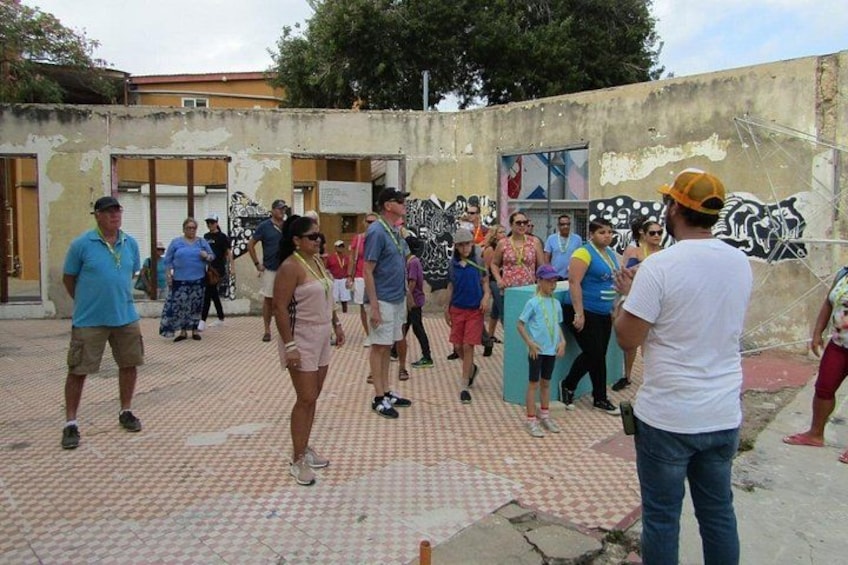 A group of people walking in an outdoor area with a patterned floor, graffiti on the walls, and a building with a door in the background. 4