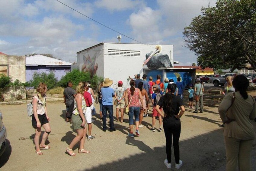 A group of people gathered outdoors, possibly at a public event or gathering, with a large mural or artwork in the background. 2