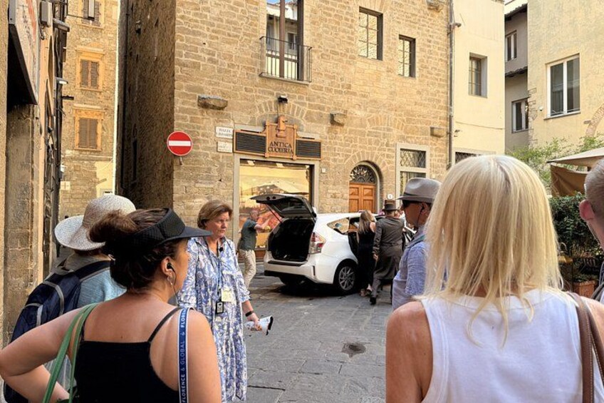 A group of people standing on a street with a white car parked in front of a building with a sign that reads 'NTICA OSTERIA.' 4