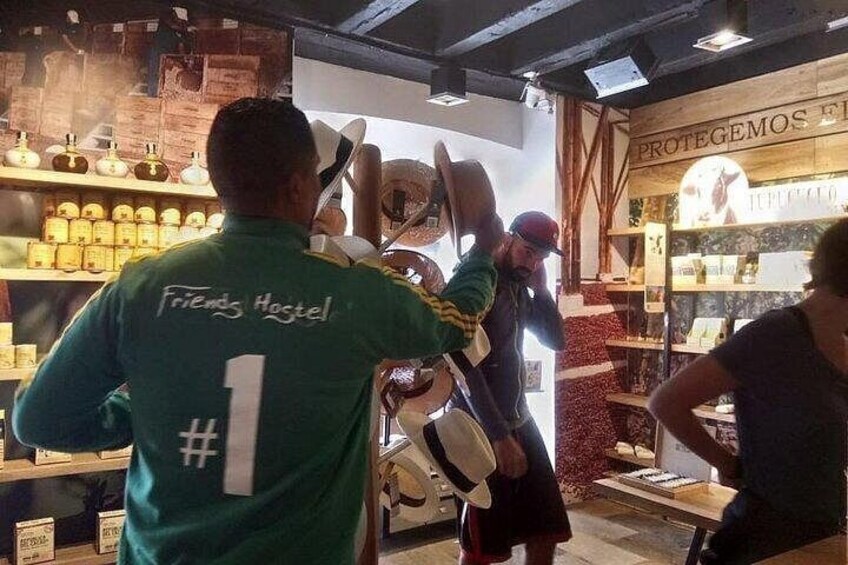 Una persona con una chaqueta verde que lleva 'Friends Hostel' y el número 1 en la espalda, parada en una tienda con estantes llenos de productos y un letrero que dice 'PROTEGEAMOS EL'. 1