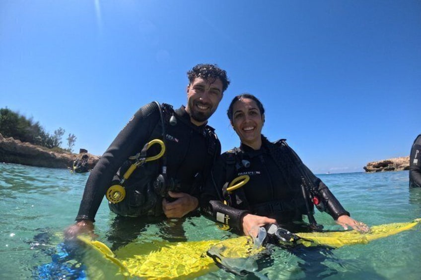 Two people in black wetsuits holding a yellow surfboard in clear water. 3