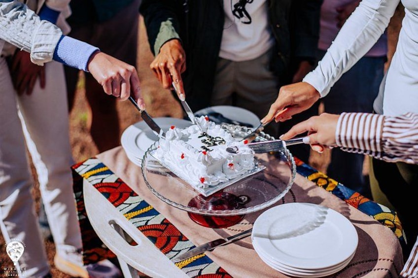 A group of people cutting a cake on a table with a colorful tablecloth. 3