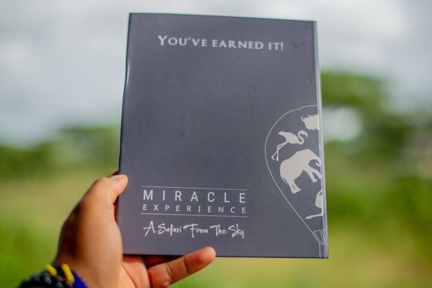 Een hand houdt een donkere doos vast met de tekst 'You've Earned It! Miracle Experience A Safari From The Sky'. 3