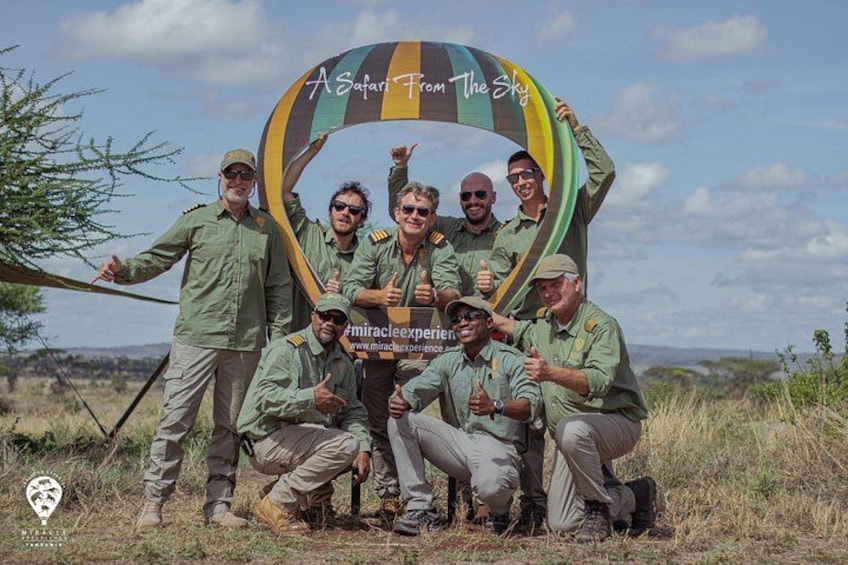 A group of people in safari uniforms posing under a colorful arch with the text 'A Safari From The Sky'. 2