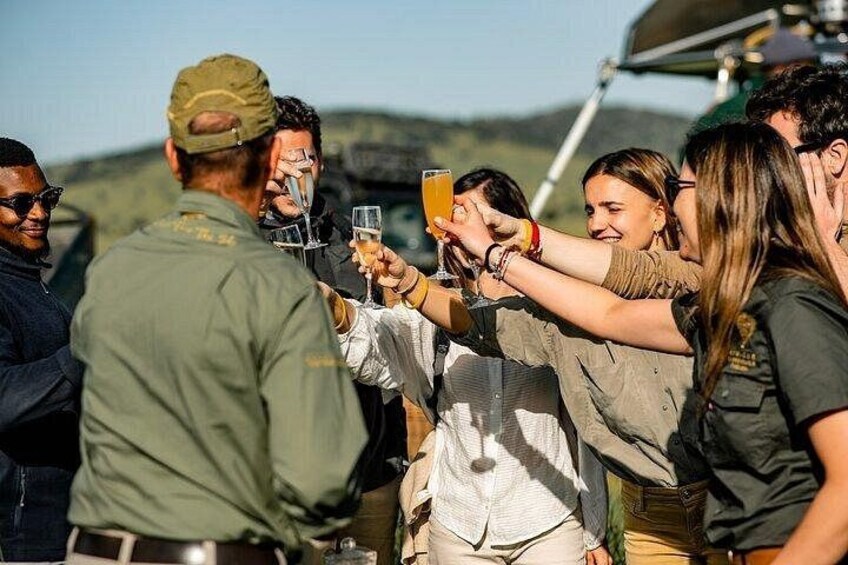 A group of people toasting with drinks, wearing casual outdoor clothing, and standing near a vehicle. 5