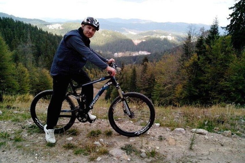 A person on a mountain bike in a forested area with a view of distant hills. 1