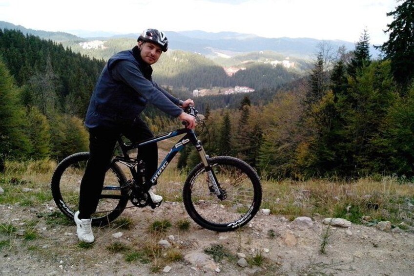 A person on a mountain bike in a forested area with a view of distant mountains. 1