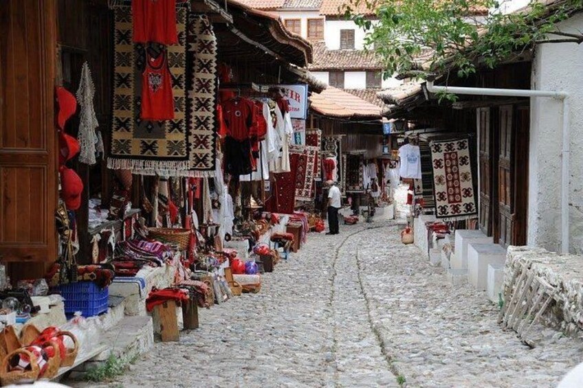A cobblestone street with shops displaying textiles and clothing. 1