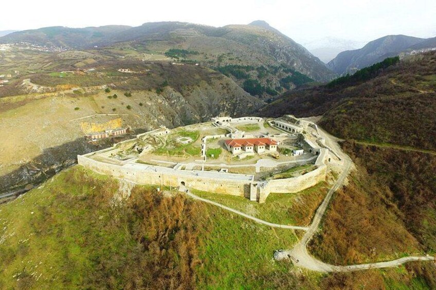 A fortified structure with a central building, surrounded by walls and a winding road. 3