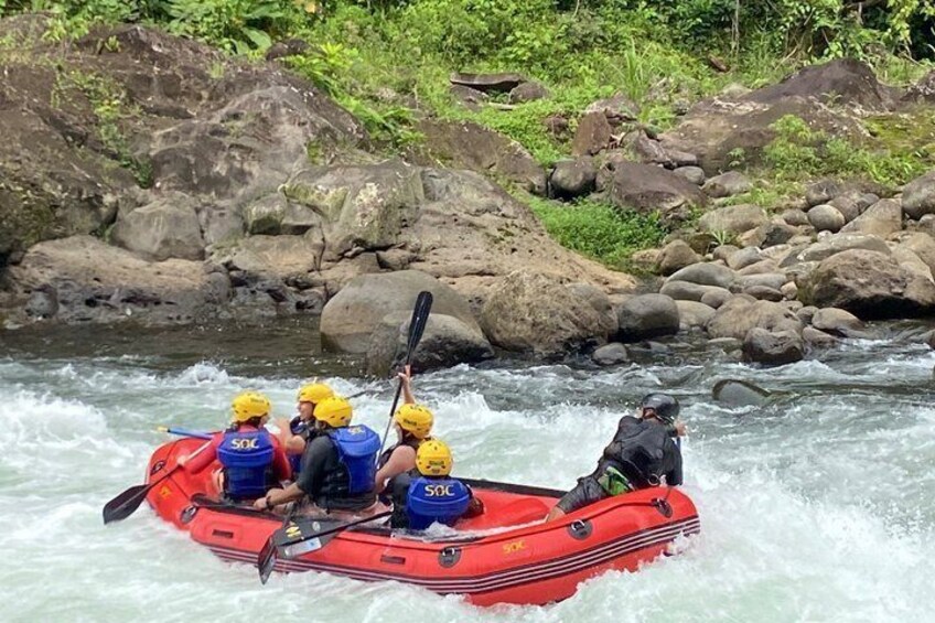 A group of people in a red raft navigating a river with rapids. 1