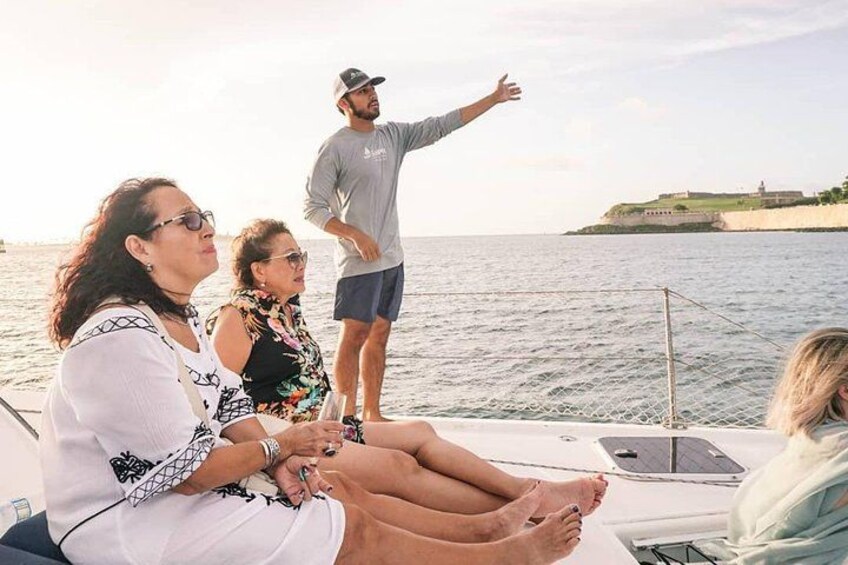 Un groupe de personnes se trouve sur un bateau. Un homme fait un geste, un ordinateur portable est posé sur la table, et un paysage côtier se dessine à l’arrière-plan. 3