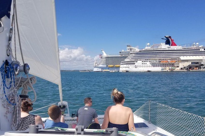 Un voilier transportant des passagers, un grand navire de croisière en arrière-plan et des eaux bleues et calmes. 2