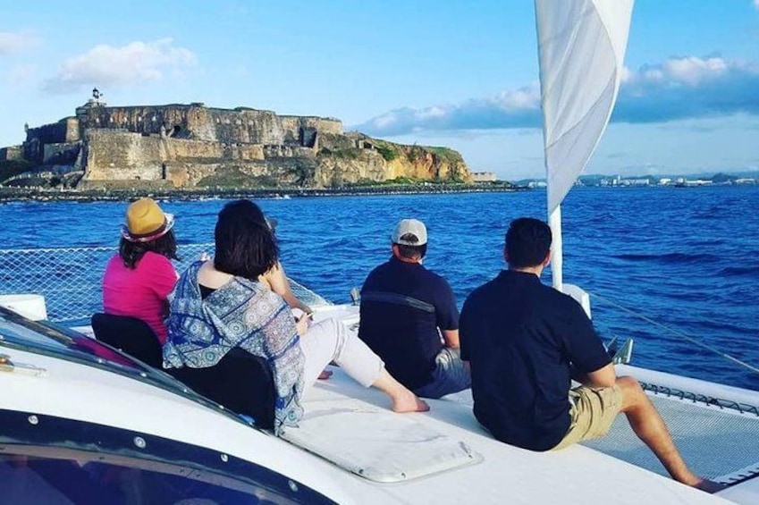 Un groupe de personnes à bord d’un voilier, avec une fortification côtière en arrière-plan. 5