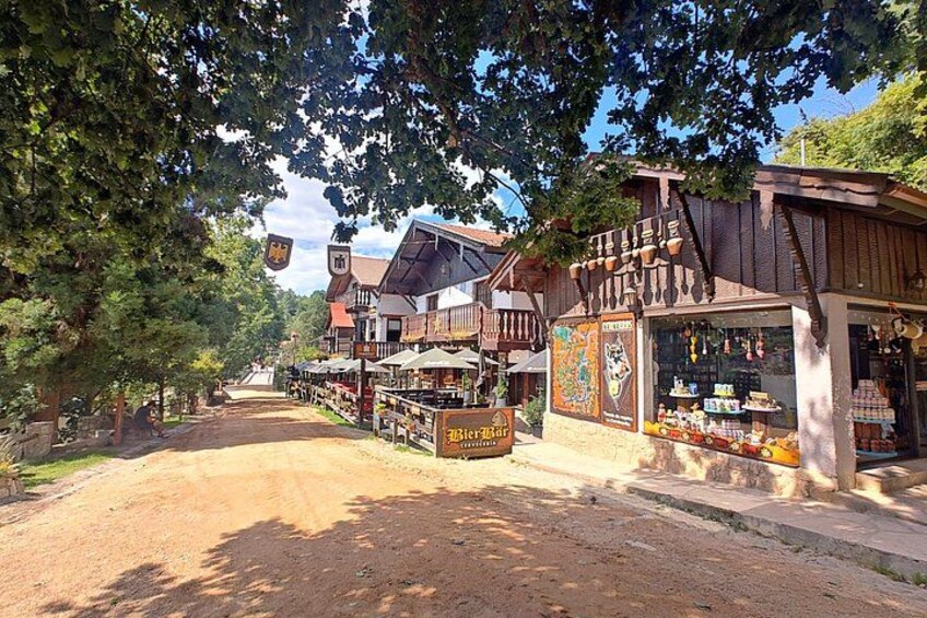 Une rue rustique bordée de bâtiments en bois, avec un chemin de terre et des arbres. 2