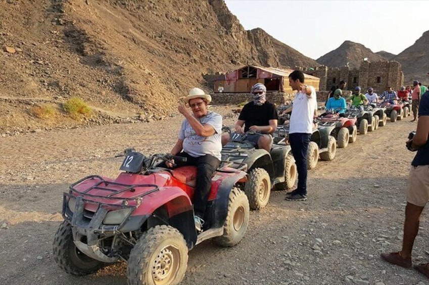 A group of people on ATVs on a dirt road with rocky terrain and mountains in the background. 2