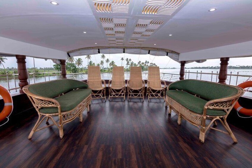A boat deck with wicker chairs and a table, surrounded by water and palm trees. 3